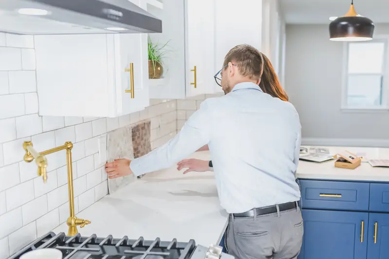 Designer holding a tile sample against the wall while a homeowner looks on