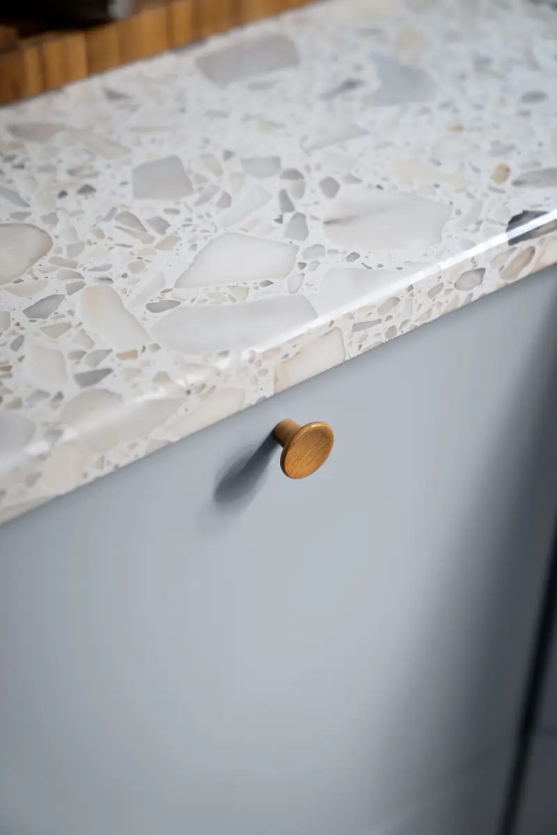 Brass knob on a gray cabinet door below a terrazzo countertop