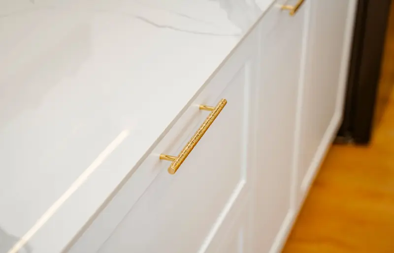 Brushed brass bar pull on a white cabinet drawer