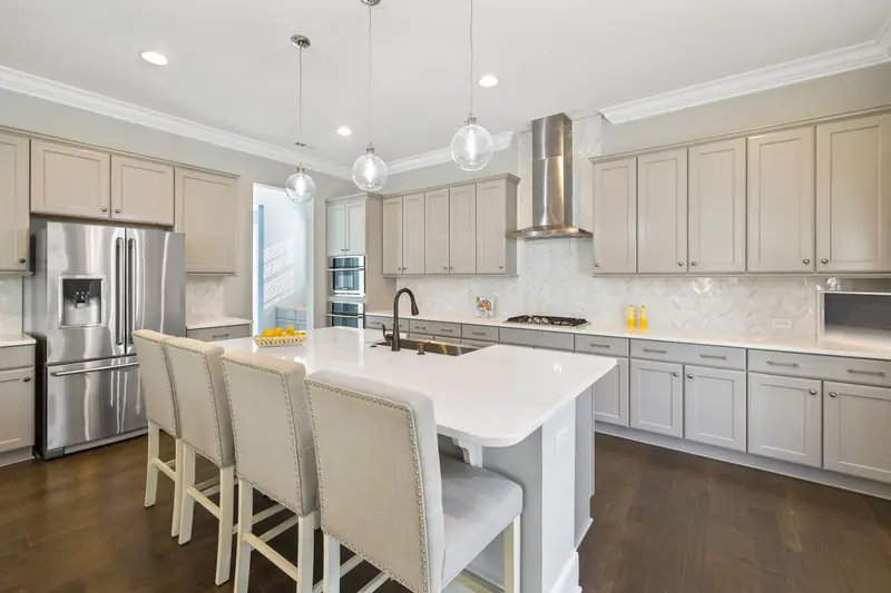 White kitchen with a large island, upholstered stools and pendant lights