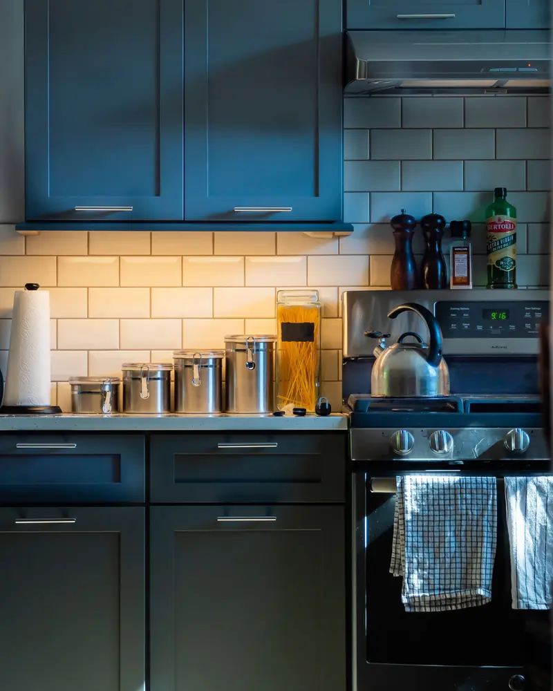 Deep blue kitchen cabinets with black hardware and a subway tile backsplash