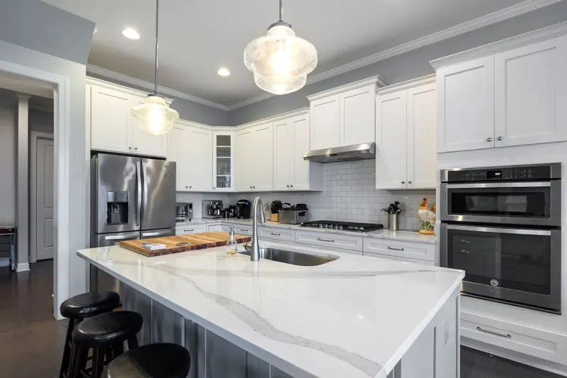 White Shaker kitchen with a quartz island and glass pendants