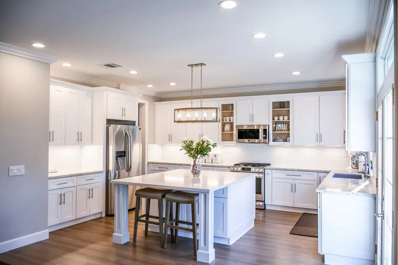 White kitchen with an island, pendant lights and dark wood floors